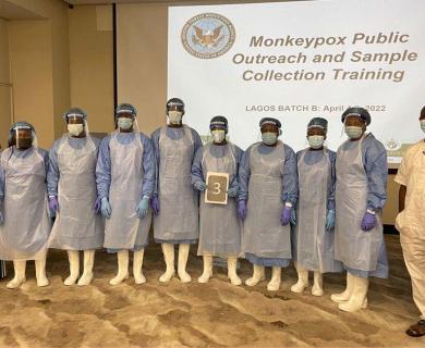 A group of students in personal protective equipment stand in front of a training presentation