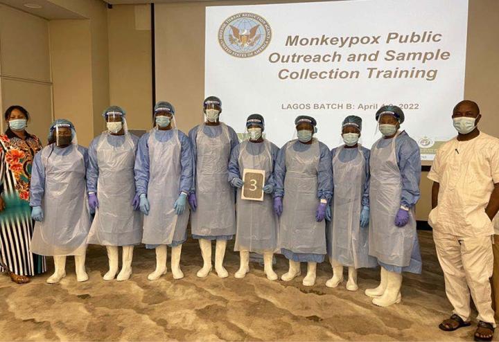 A group of students in personal protective equipment stand in front of a training presentation