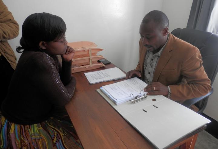 A man and a woman consult documents in a binder at a desk