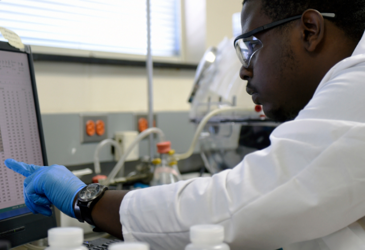 Black man in lab gear looks at computer screen at research laboratory 