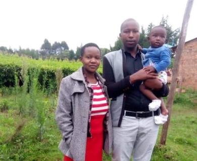 Joyline stands outside with her husband and infant son.