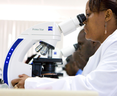 Kenyan woman studies a microscope next to several of her fellow students at the Kenyan Medical Research Institute