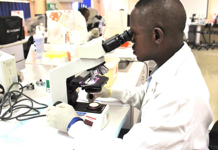 A man in a white lab coat looks into a microscope.