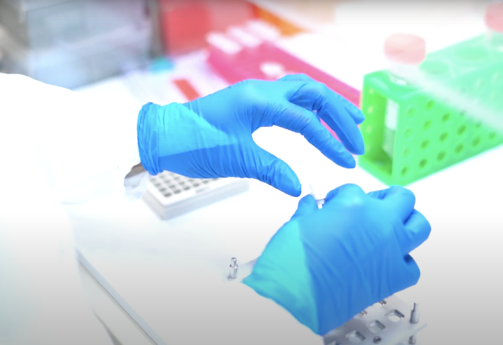 Close up of gloved hands handling vials at a lab bench