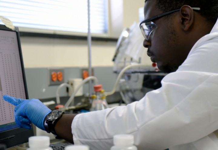 Black man in lab gear looks at computer screen at research laboratory