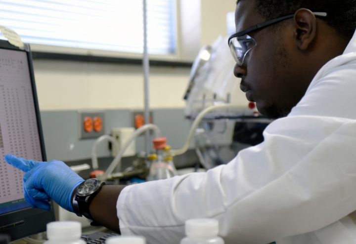 Black man in lab gear looks at computer screen at research laboratory 