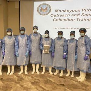 A group of students in personal protective equipment stand in front of a training presentation